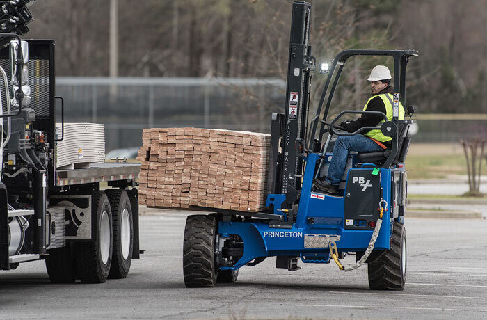 man driving a princeton piggyback forklift. He is loading lumber onto the back of a truck